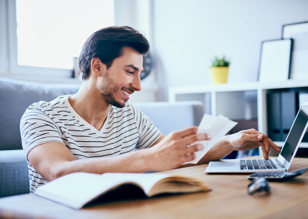 financial advisor smiling as he holds paperwork and looks at a laptop screen